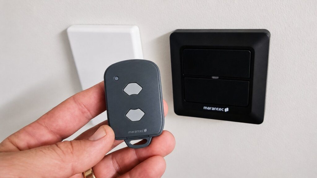 Garage and gate remote held in hand beside a wall button during programming setup